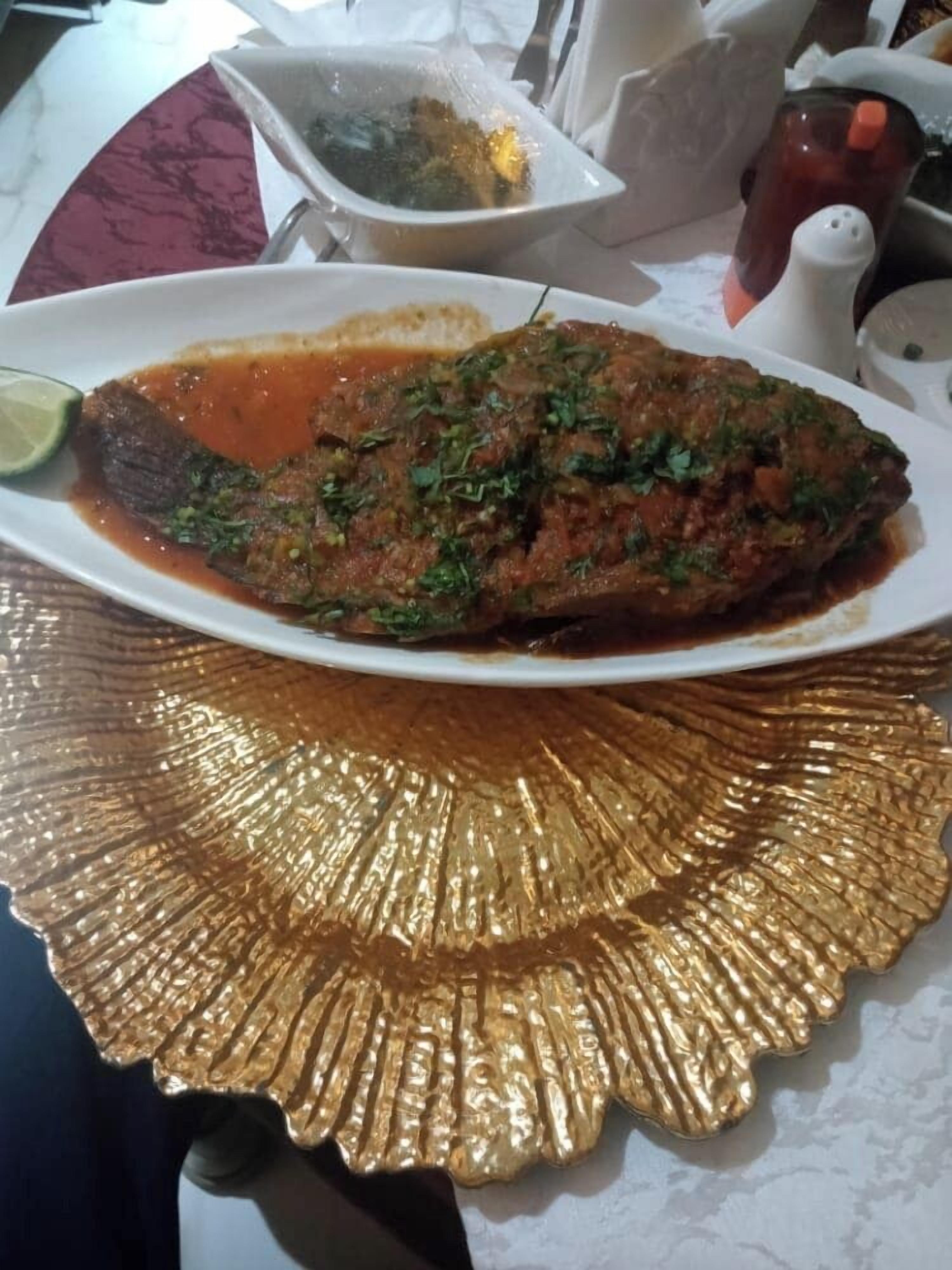 Un plato de pescado sobre un plato blanco con un plato decorativo dorado debajo.
