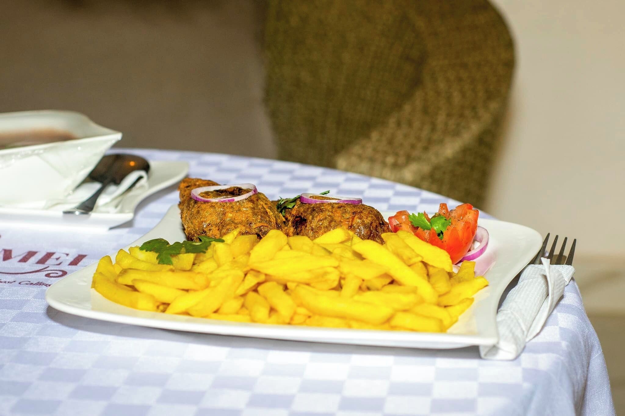 Une assiette de nourriture comprenant des frites et un plat de viande, peut-être du poulet frit, garnie d’oignons et d’herbes, posée sur une table recouverte d’une nappe à carreaux.