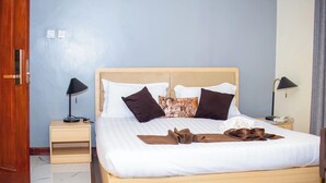 Una cama bien hecha con cabecera de madera, dos mesitas de noche con lámparas y un armario de madera.