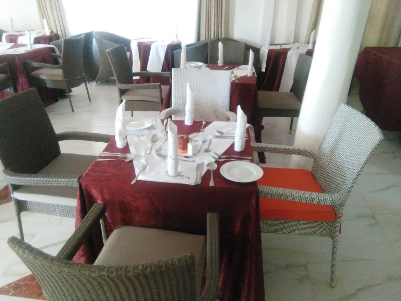 A dining area with tables set for two, featuring wicker chairs and red tablecloths.