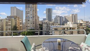 Un balcón con una mesa y sillas de vidrio, con vista a un paisaje urbano con diversos edificios.