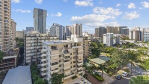 Un edificio residencial alto con varios balcones, rodeado de otros edificios altos y palmeras.