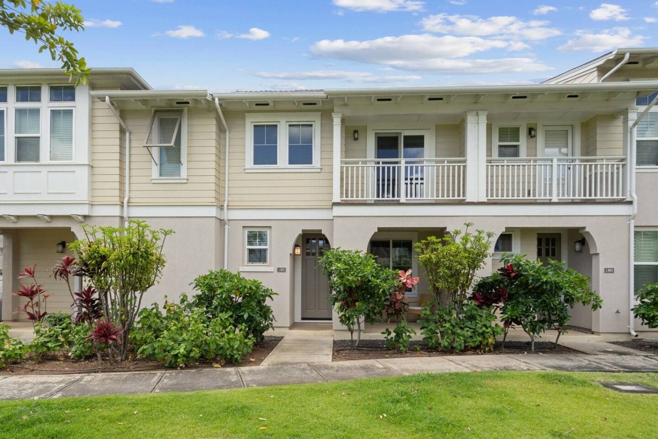 A row of townhouses with a front porch, a small garden area, and a clear sky.