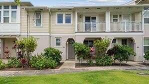 A row of townhouses with a front porch, a small garden area, and a clear sky.