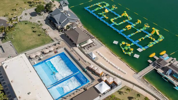 An aerial view of a resort with a large swimming pool, a water park, and a building with a sloped roof.
