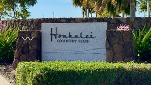A sign for Hoakalei Country Club with a stone wall and palm trees in the background.