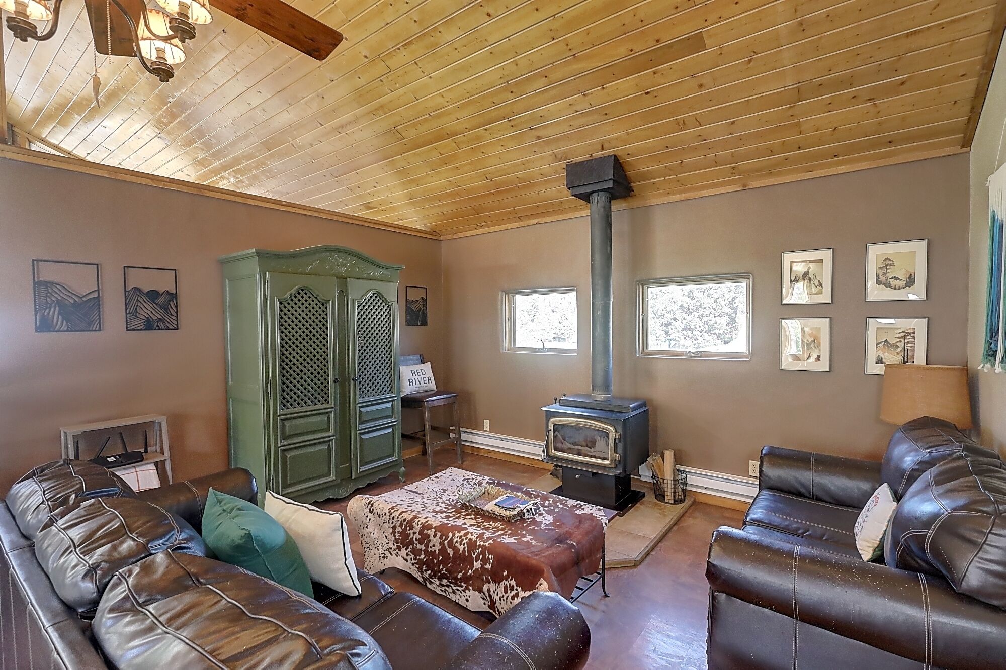 A cozy living room with leather sofas, a green cabinet, a wood-paneled ceiling, and a wood-burning stove.