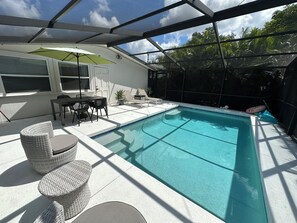 Piscina exterior cubierta con mesa y sillas, rodeada por una valla blanca y plantas en macetas.