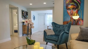 A modern living room with a blue armchair, a glass coffee table with candles, and a painting on the wall. - Beautifully Remodeled Home with Pool Near Siesta (Sarasota)