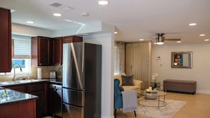 A modern kitchen with a stainless steel refrigerator, a dishwasher, and a built-in oven. There is a dining area with a round table and a bench. The living room has a sofa and a coffee table. - Beautifully Remodeled Home with Pool Near Siesta (Sarasota)