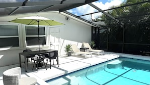 A covered outdoor pool area with a table and chairs, a potted plant, and a door. - Beautifully Remodeled Home with Pool Near Siesta (Sarasota)