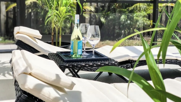 A sunlit outdoor seating area with a bottle and glass on a tray, surrounded by lush greenery. - Beautifully Remodeled Home with Pool Near Siesta (Sarasota)