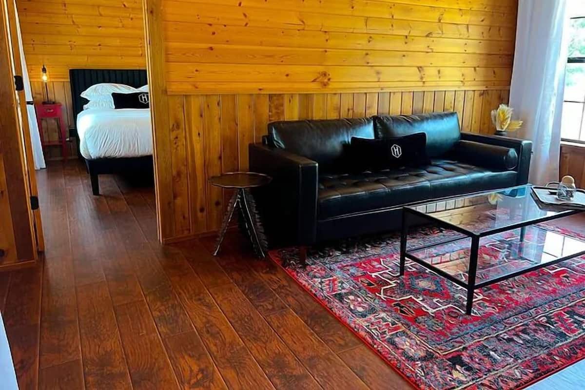 A wooden-paneled room with a black leather sofa, a glass coffee table, and a patterned rug.