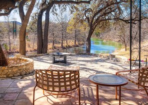 An outdoor patio with a table and chairs, a stone planter, and a view of a body of water. - Luxury Home on 100 acre Secluded Ranch, Waterfront, Little Frio Creek (Leakey)