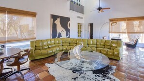 A modern living room with a green leather sectional sofa, a glass coffee table, and a cowhide rug. - Luxury Home on 100 acre Secluded Ranch, Waterfront, Little Frio Creek (Leakey)