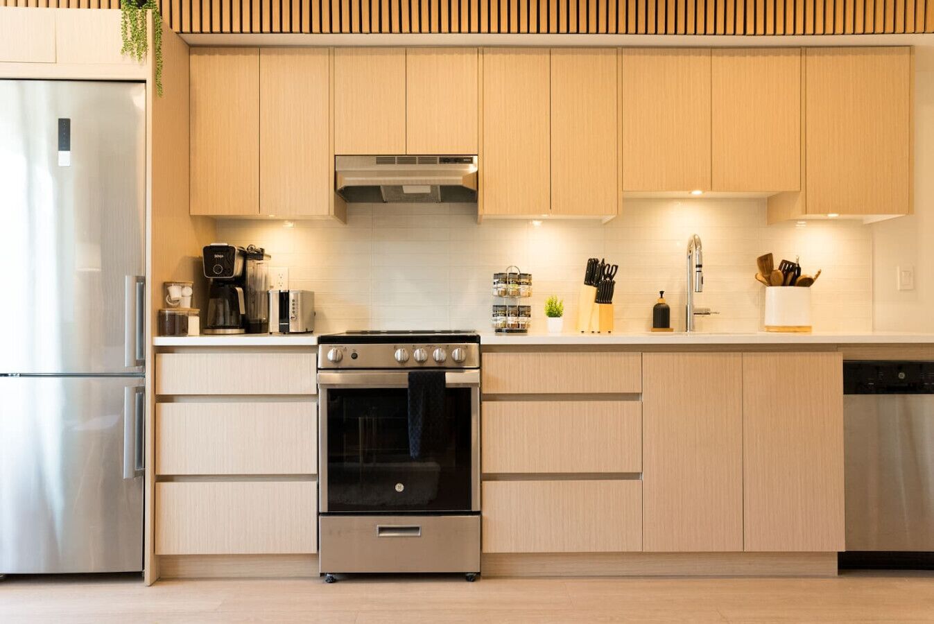 Una cucina moderna con mobili chiari in legno, elettrodomestici in acciaio inossidabile e un'isola centrale con lavello e piano di lavoro.