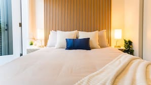 A large bed with white and blue pillows, a wooden slat headboard, and a bedside table with a lamp. - Luxury Scandinavian Suite| Cozy and Bright (North Vancouver)