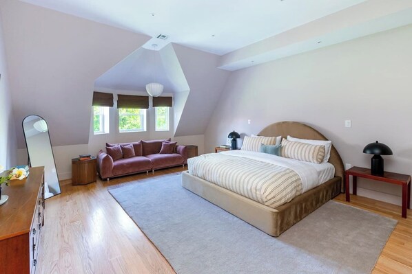 A bedroom with a large bed, a sofa, a mirror, and a nightstand.
