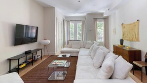 Un salon moderne avec un canapé d’angle, un téléviseur à écran plat, une table basse et une bibliothèque.