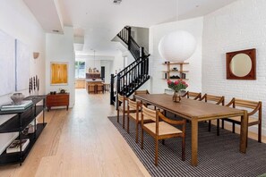 A spacious dining area with a wooden table and chairs, a staircase, and a white brick wall.