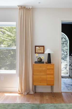 A room with a wooden cabinet, a framed picture, a vase with flowers, and a lamp.