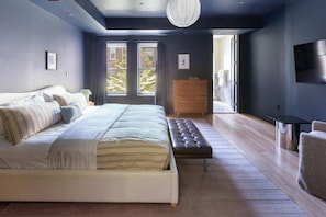Un dormitorio moderno con una cama grande, un banco, un aparador y un televisor en la pared.