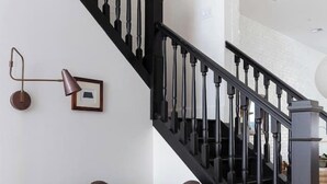 Un escalier avec des balustrades noires, un fauteuil gris et une lampe fixée au mur.