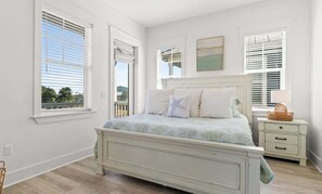 Quarto com cama, mesa de cabeceira, janela com persianas e um quadro na parede.