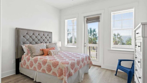A bedroom with a tufted headboard, a bed with patterned bedding, a small blue chair, and a white dresser. - Sol Shine Gulf-View Retreat Steps from the Sand (Mexico Beach)