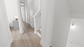 A hallway with white walls and wooden flooring, leading to a staircase. - Sol Shine Gulf-View Retreat Steps from the Sand (Mexico Beach)