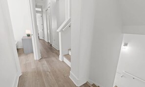 A hallway with white walls and wooden flooring, leading to a staircase. - Sol Shine Gulf-View Retreat Steps from the Sand (Mexico Beach)