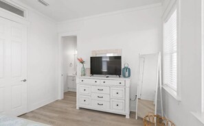 Een slaapkamer met een witte dressoir, een flatscreen-tv en een raam met zonwering.