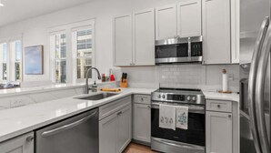 A modern kitchen with white cabinets, stainless steel appliances, and a large window providing natural light.