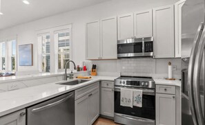 Una cocina moderna con armarios blancos, electrodomésticos de acero inoxidable y un amplio ventanal que proporciona luz natural.