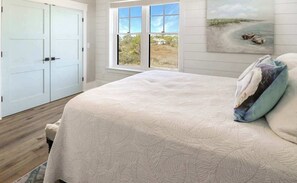 A bedroom with a large bed, a window with a view of the outdoors, and a door to the left.