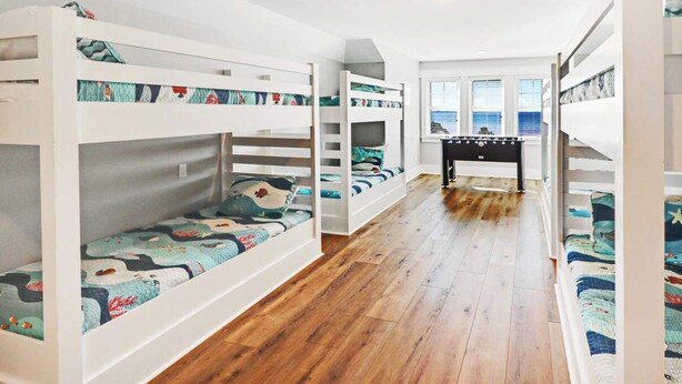 Dormitorio con literas, suelo de madera, una mesita y vistas al mar a través de amplias ventanas.