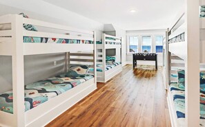 Dormitorio con literas, suelo de madera, una mesita y vistas al mar a través de amplias ventanas.