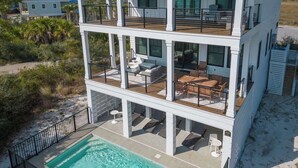 Una casa frente al mar de varios pisos con piscina, mobiliario exterior y balcón.