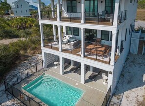 Una casa frente al mar de varios pisos con piscina, mobiliario exterior y balcón.