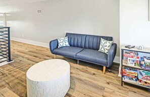 A modern living room with a blue sofa, two patterned pillows, a round wooden coffee table, and a shelf with board games.