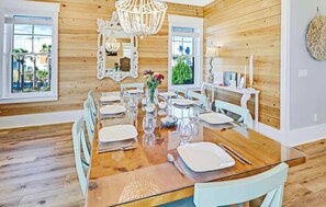 A dining area with a wooden table set for six, surrounded by white chairs.