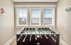 Una mesa de fútbol de mesa en una habitación con tres ventanas y obras de arte en las paredes.