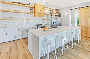 Una cocina moderna con una isla grande, muebles blancos, estantes de madera y una puerta corrediza tipo granero.