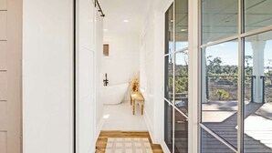 Un pasillo estrecho con piso de madera, pared blanca y un gran ventanal que da a una terraza exterior.