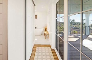 Un pasillo estrecho con piso de madera, pared blanca y un gran ventanal que da a una terraza exterior.