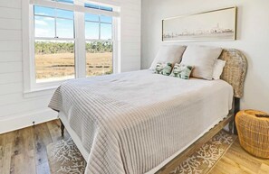 Un dormitorio con una cama grande, vista al exterior a través de una ventana y un cuadro enmarcado en la pared.