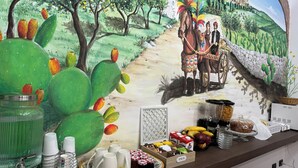 A buffet setup with a mural, including a cactus, a tray with food items, and a beverage dispenser.