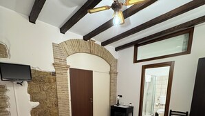 A bedroom with two beds, a ceiling fan, a TV, and a bathroom visible through an open door.
