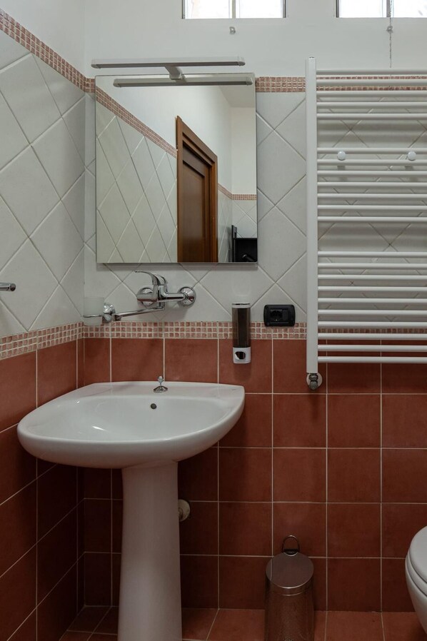 Casa de banho com lavatório suspenso, espelho, porta-toalhas e sanita.