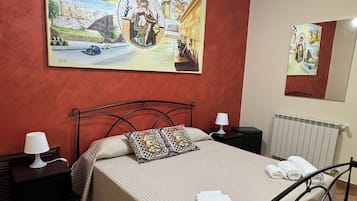 Un dormitorio con una cama, mesitas de noche, ventilador de techo y un cuadro grande en la pared.
